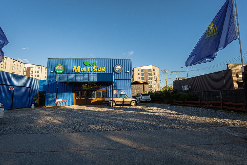 Frente del galpón azul de Multisur, con su estacionamiento de ripio